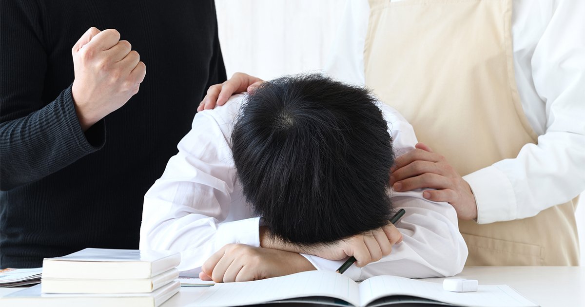 机に頭を伏せる子供と励ます母親と父親