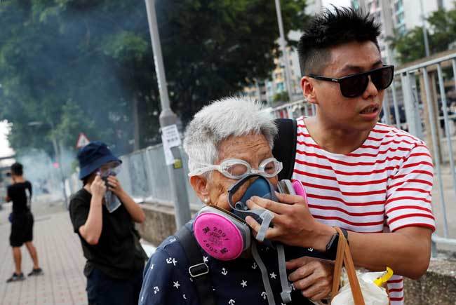 香港で警察が放った催涙ガスから身を守るよう通行人を助けるデモ参加者