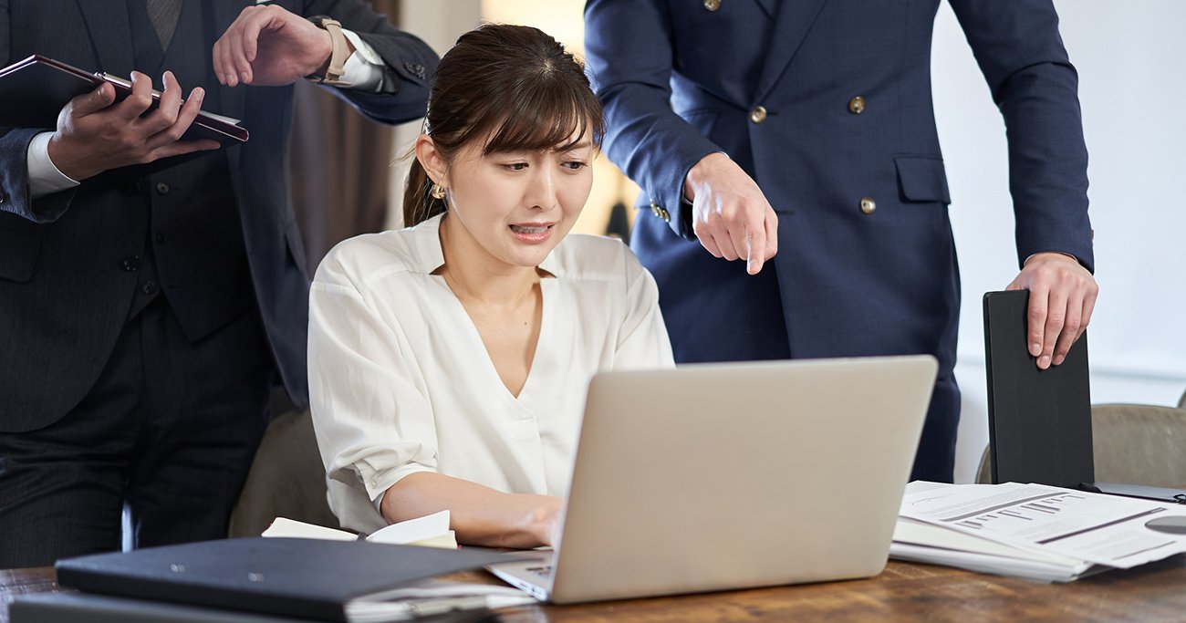パソコンを前に複数の人から指示を受ける女性