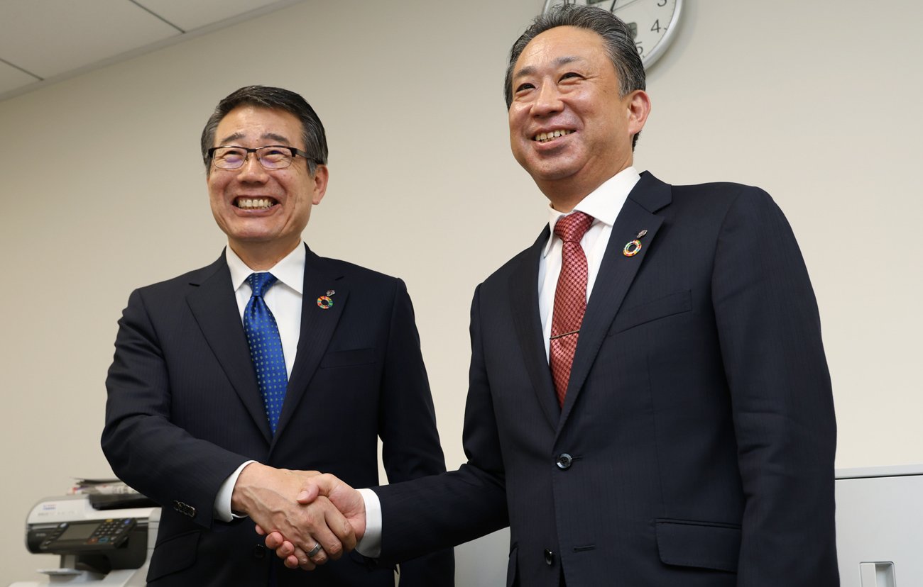 握手する永松文彦社長と阿久津知洋執行役員