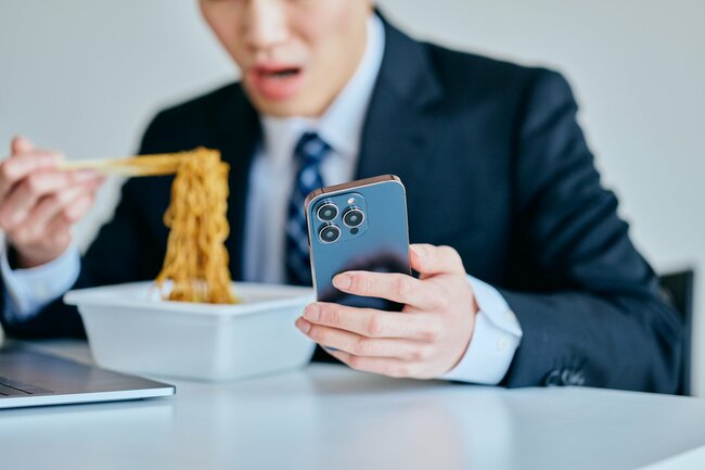 スマホを操作しながらカップ麺を食べる男性