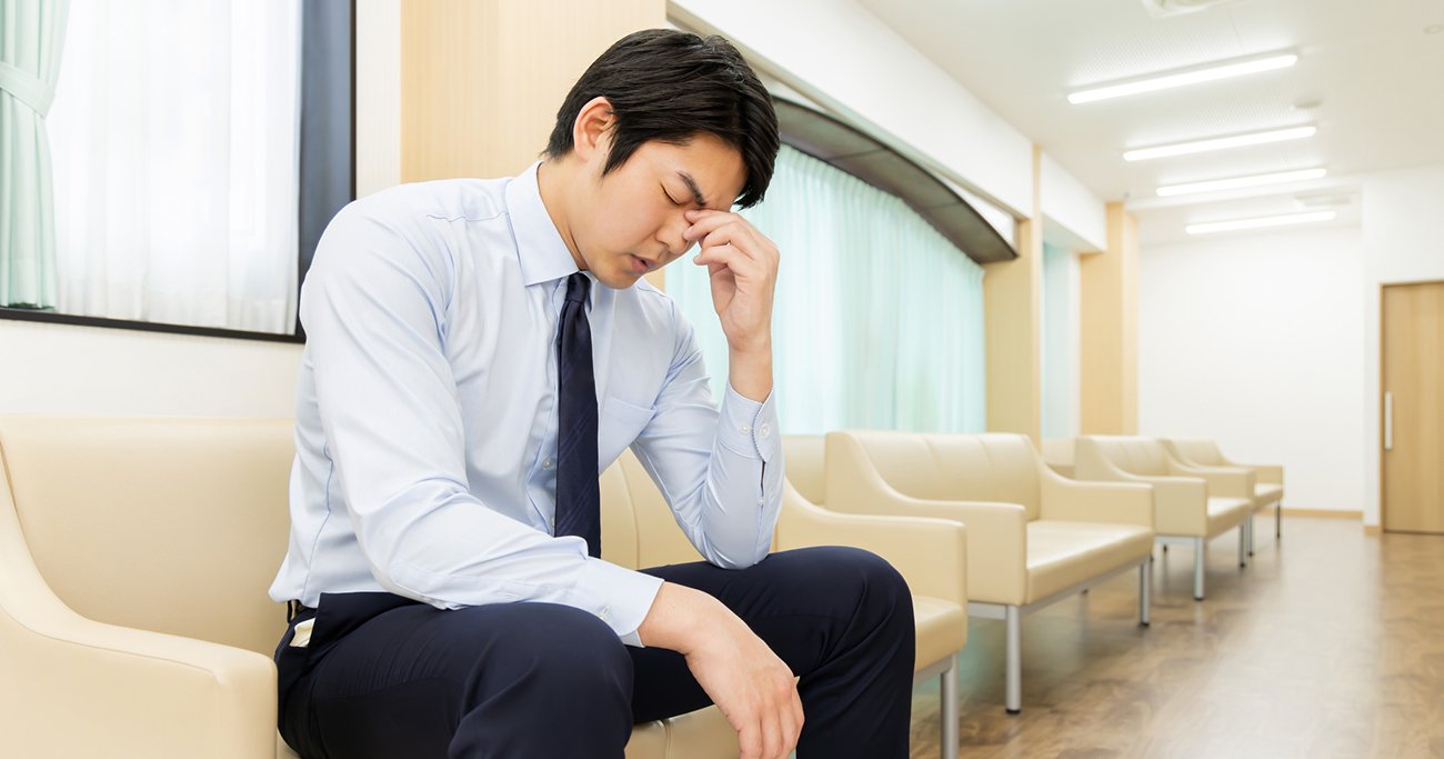 待合室で額に手を当てて座る男性