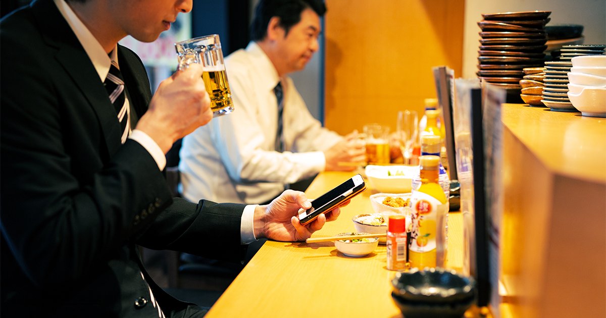 カウンターでビールを飲みながらスマホを操作するビジネスパーソン