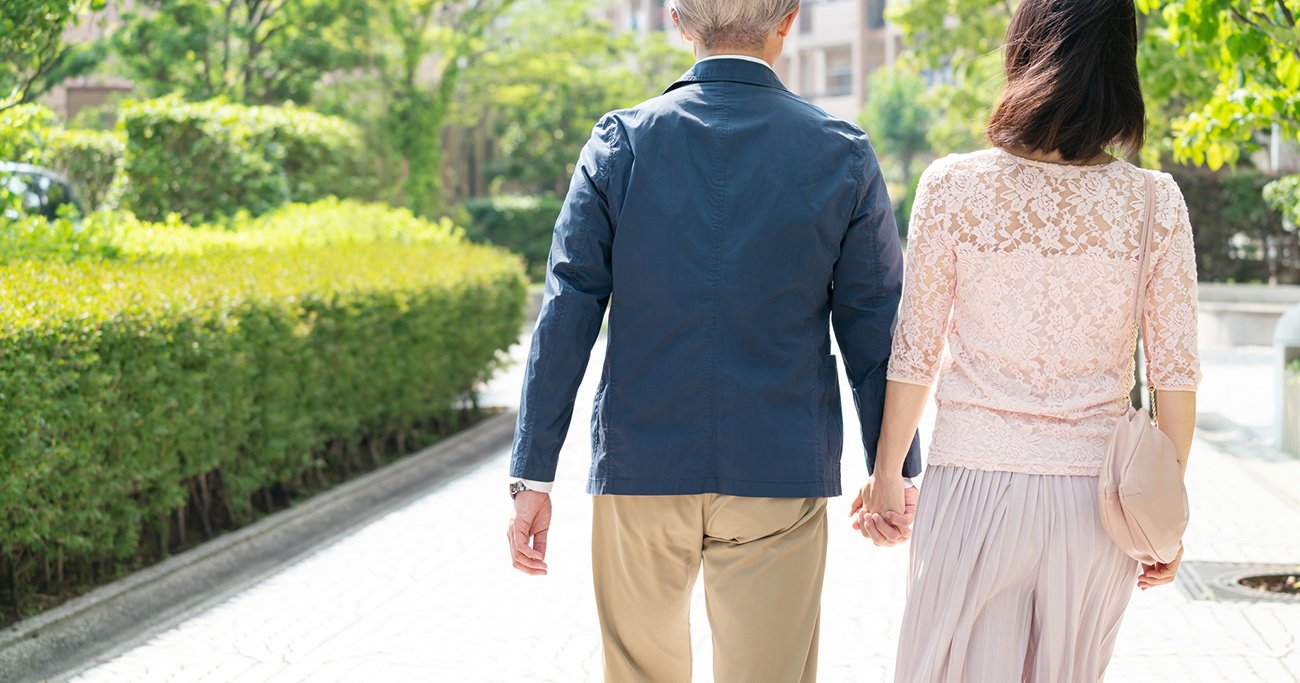 緑道を手をつないで散歩する高齢の夫婦の後ろ姿
