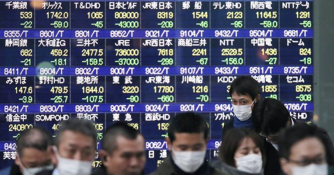 株価下落を示す株価ボードとマスクをする人々