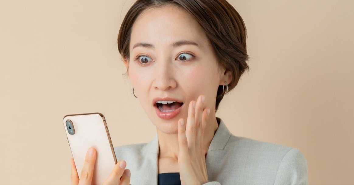 スマホの画面を見て驚く女性