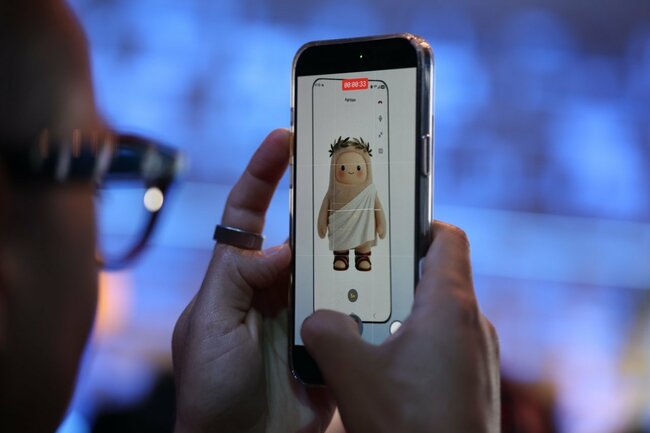 メタのスマートグラスを装着し、画面上に表示されたAIエージェント「ミューズ」を動画で撮影する来場者