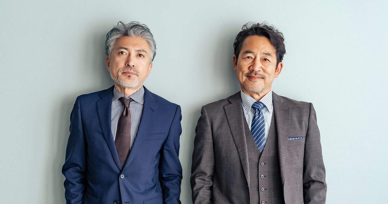 スーツ姿の中高年男性2人が並んで立つ様子