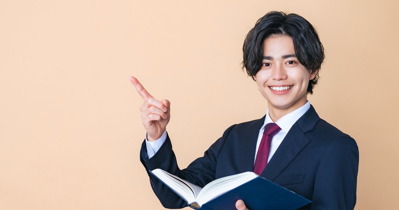 本を持ちながら笑顔で指を差すビジネスマン