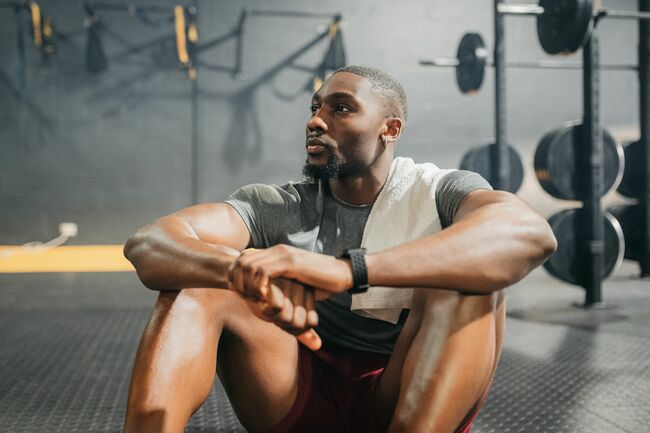 relax, thinking and black man in training gym resting his body after weightlifting workout muscular, healthy and strong fitness person on exercise break thoughtful while relaxing on floor