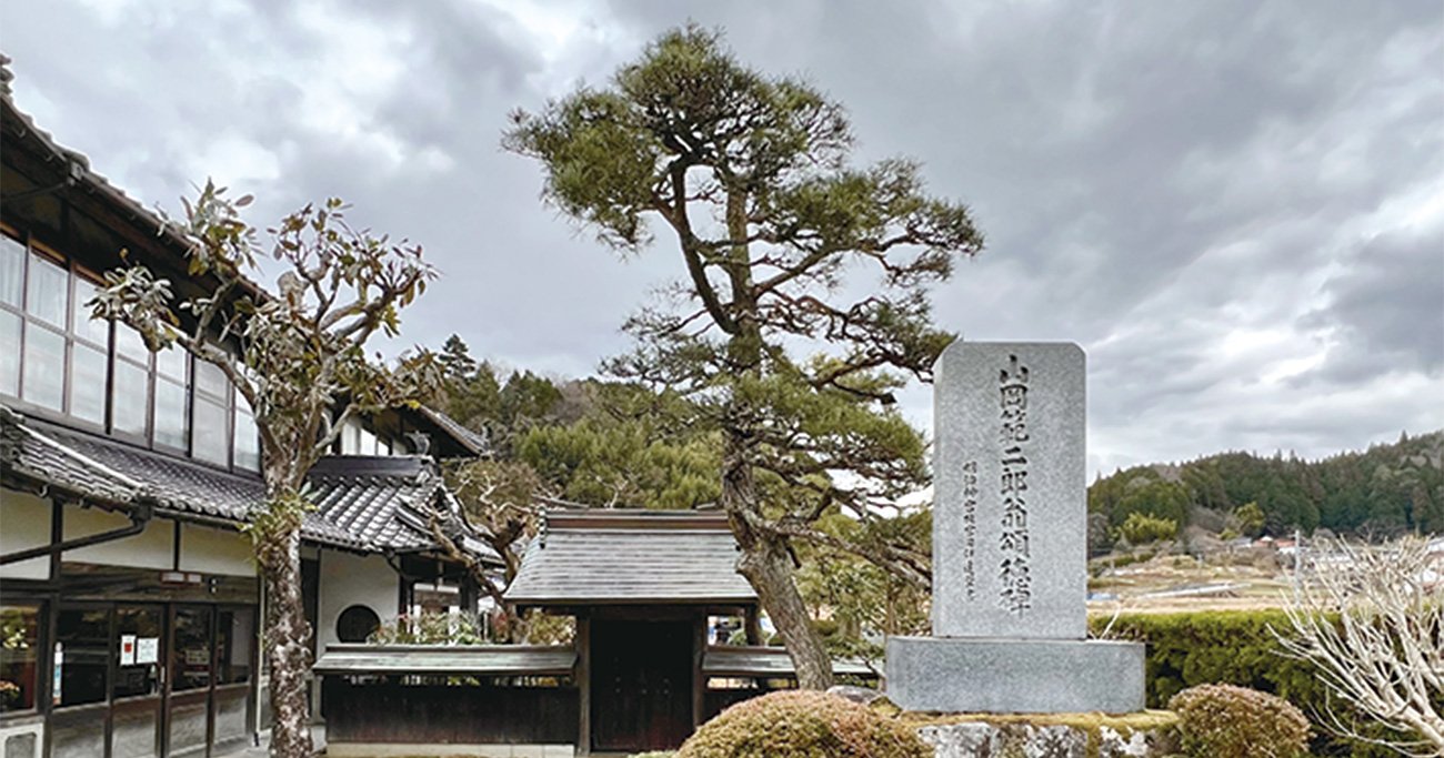 a蔵外観。山岡克巳さんの曽祖父で酒造り初代の範二郎さんの石碑も