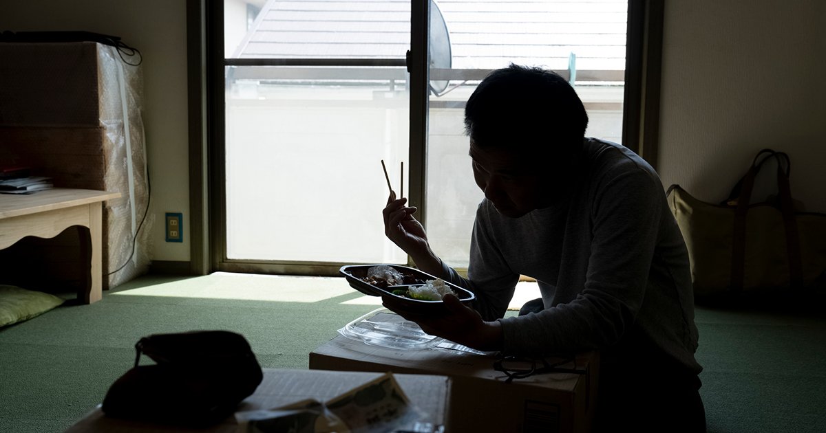 暗い部屋で弁当を食べる男性