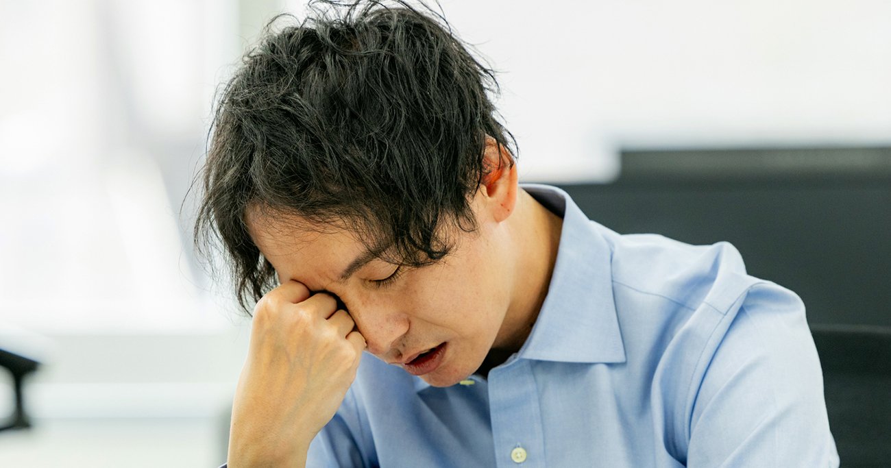 頭を抱え疲れた表情を見せる男性会社員