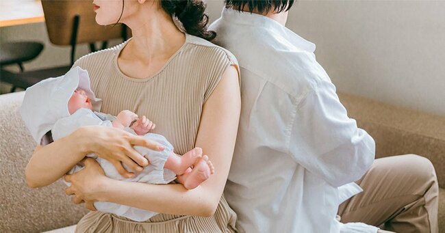 赤ちゃんを抱く母親と背中合わせの父親