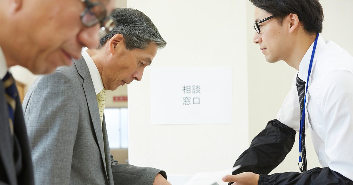 窓口で説明を受けているスーツ姿のシニア男性