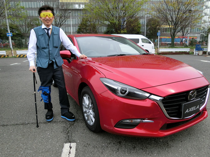 マツダによる高齢ドライバー体験の様子。専用のアイマスクで視野を狭め、サポーターで膝や肘の動きを抑え、重りを入れた靴を履く。マツダ関係者が筆者を撮影