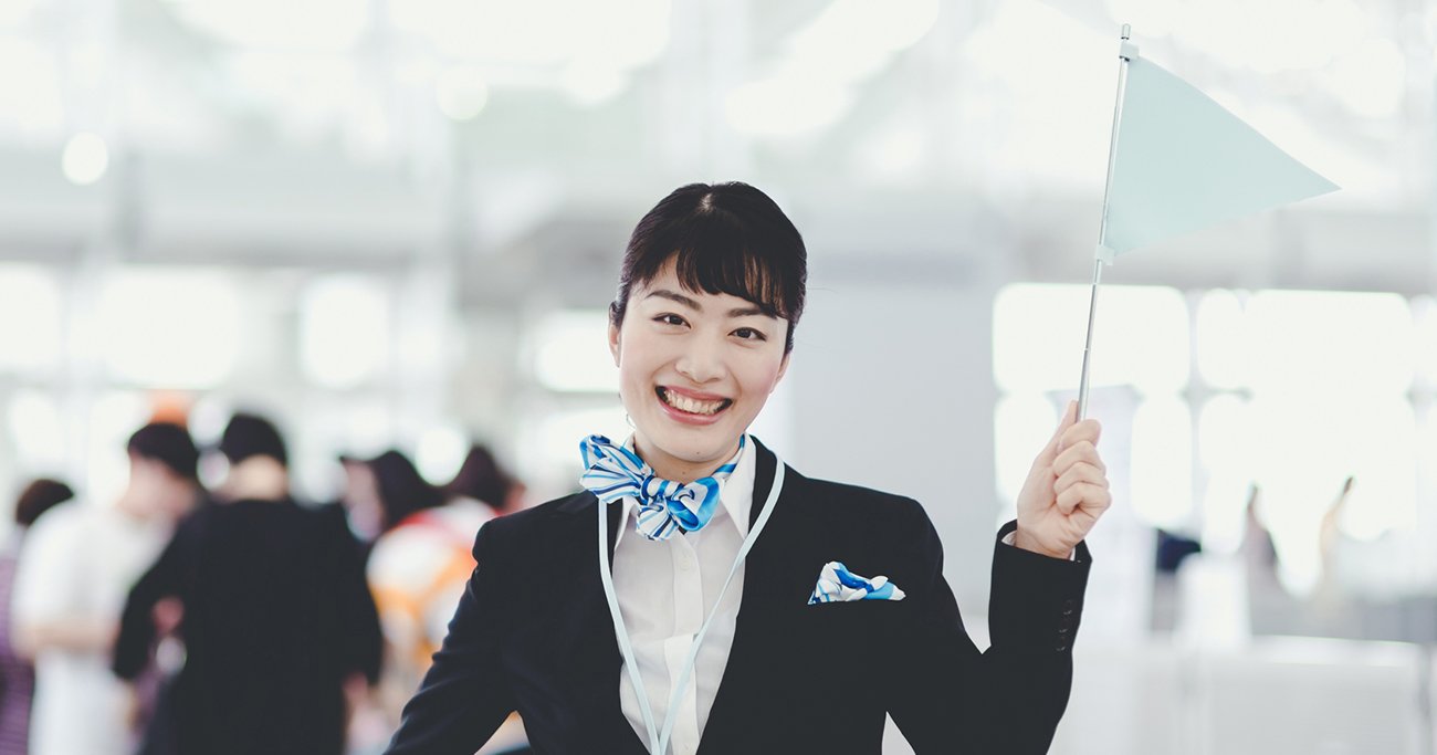 案内用の小旗を持ち笑顔で立つ女性スタッフ