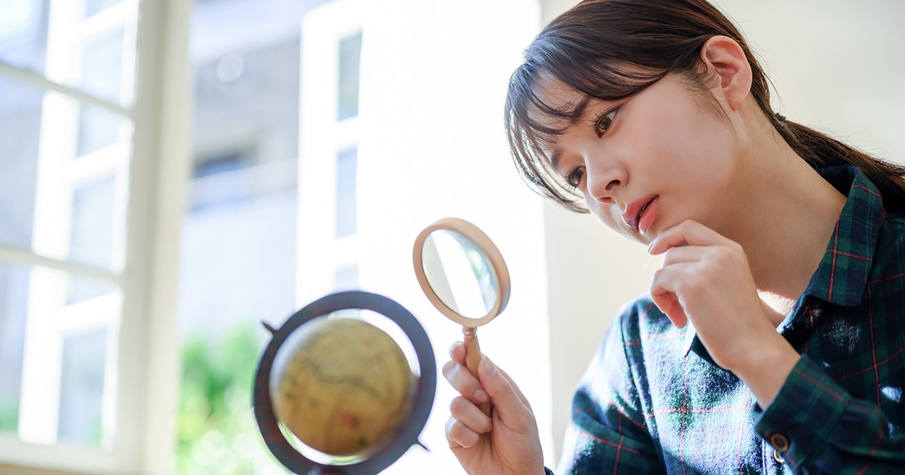 虫眼鏡で地球儀を観察する女性