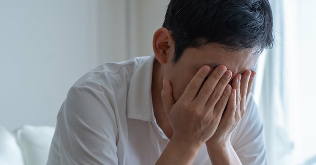 手で顔を押さえソファに座る男性