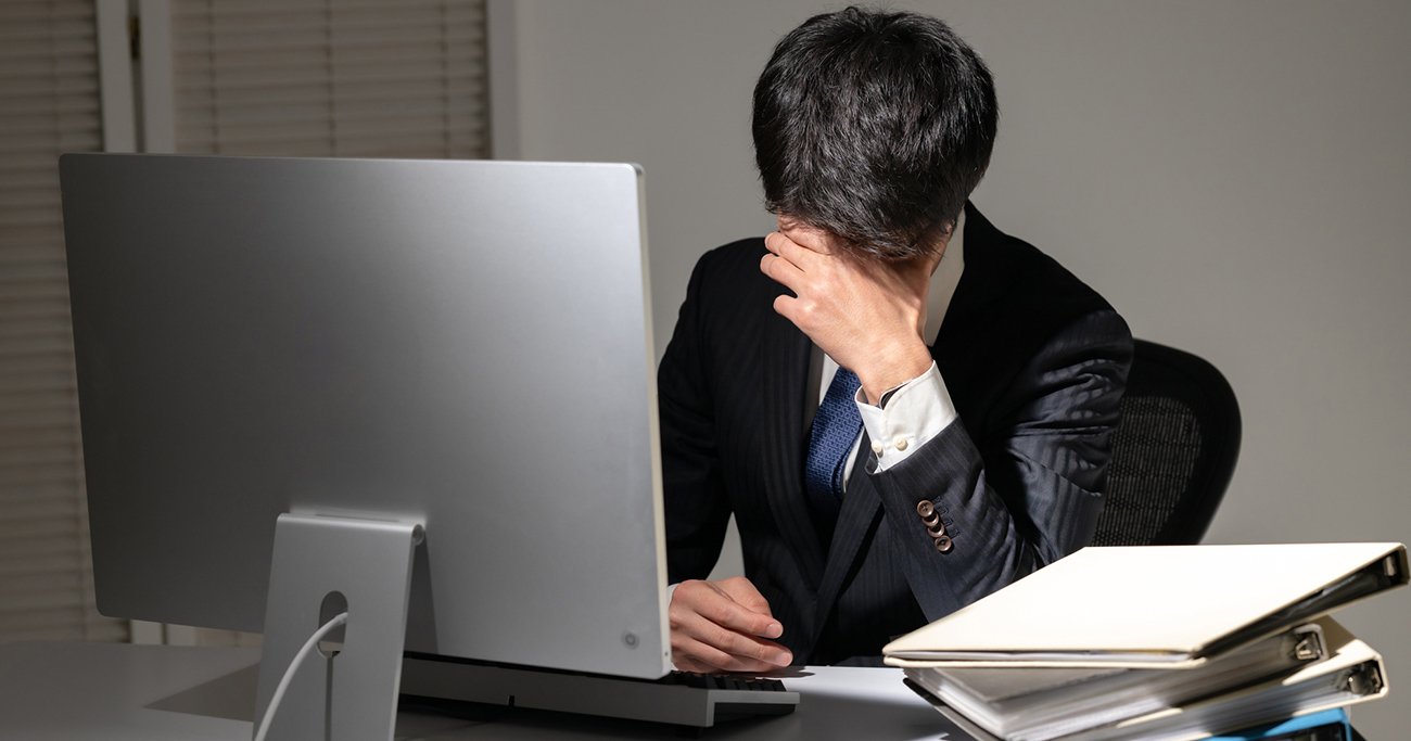 パソコンの前で顔を覆うスーツ姿の男性