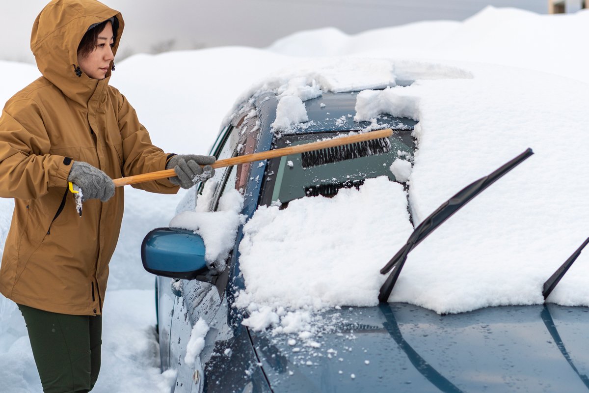 車に積もった雪を下ろす若い女性