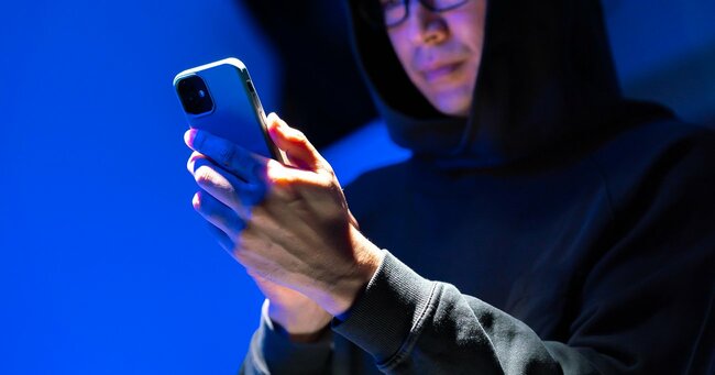 スマートフォンを操作するフード姿の人物