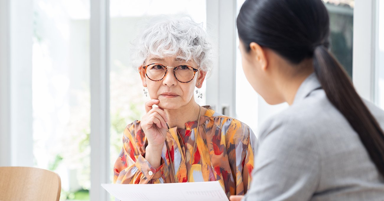 資料を見ながら話を聞く高齢女性と担当者