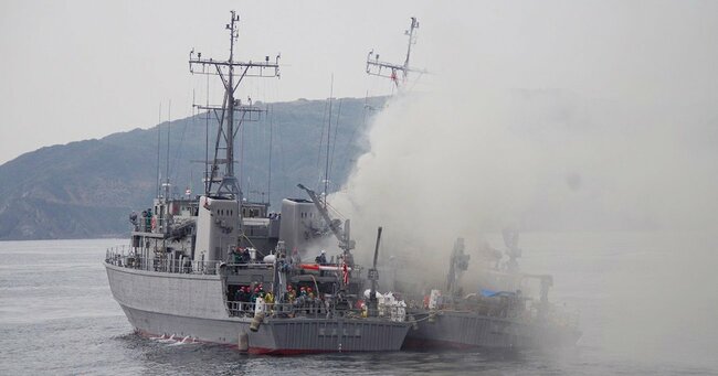 火災の煙で覆われる海上自衛隊の掃海艇「うくしま」と、消火活動に当たる「とよしま」