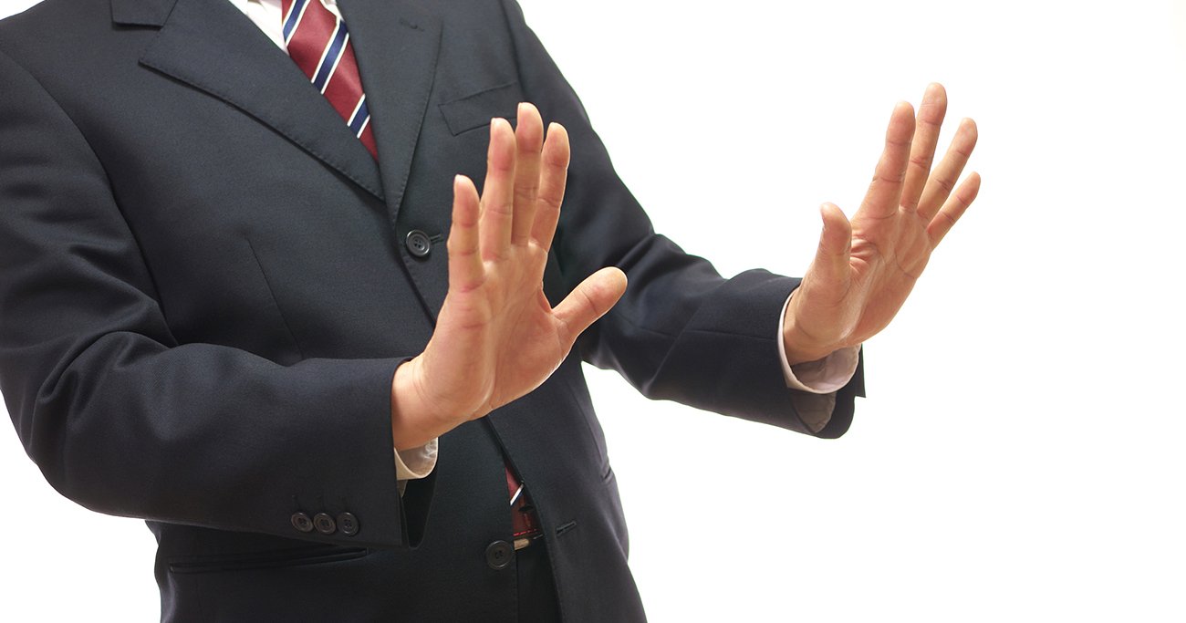 両手を前に出して断るしぐさをするスーツ姿の男性