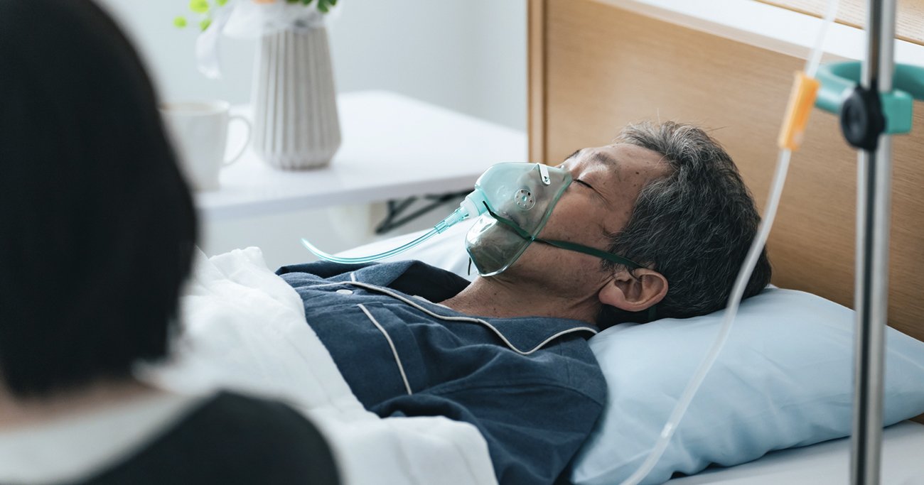 病床で酸素マスクをつける高齢男性