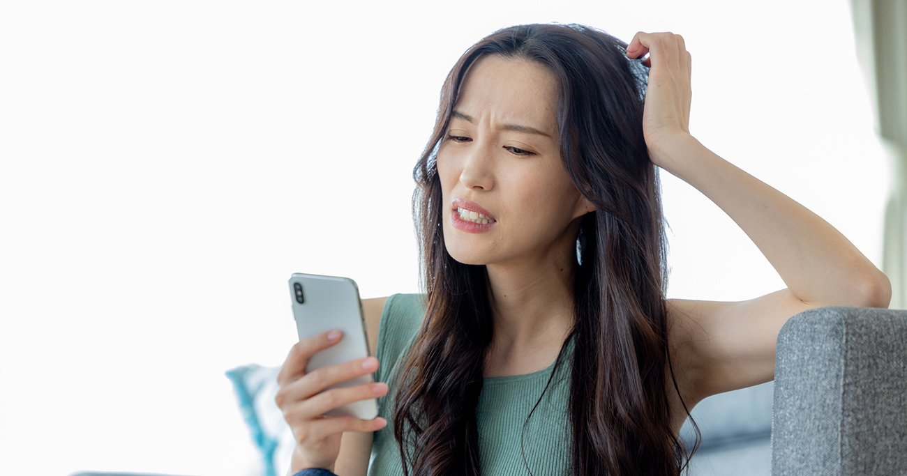 スマートフォンを見ながら困った表情をする女性