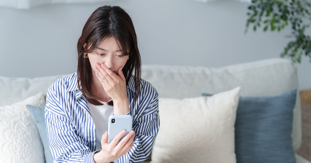 スマートフォンを見ながら口元を押さえる女性
