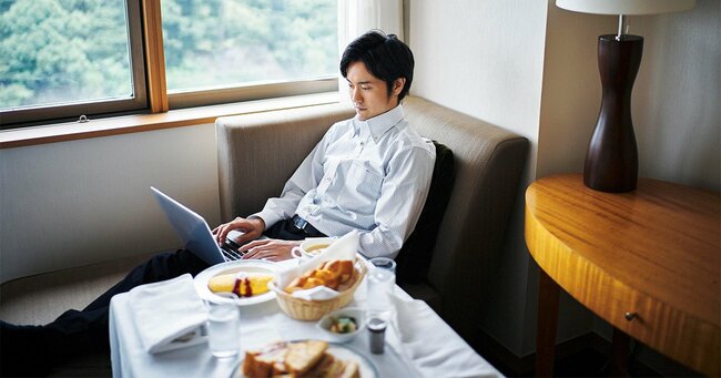 ホテルの自室で朝食をとる男性