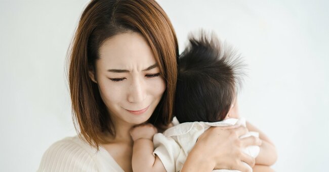 赤ちゃんを抱えて、疲れた表情をするお母さん