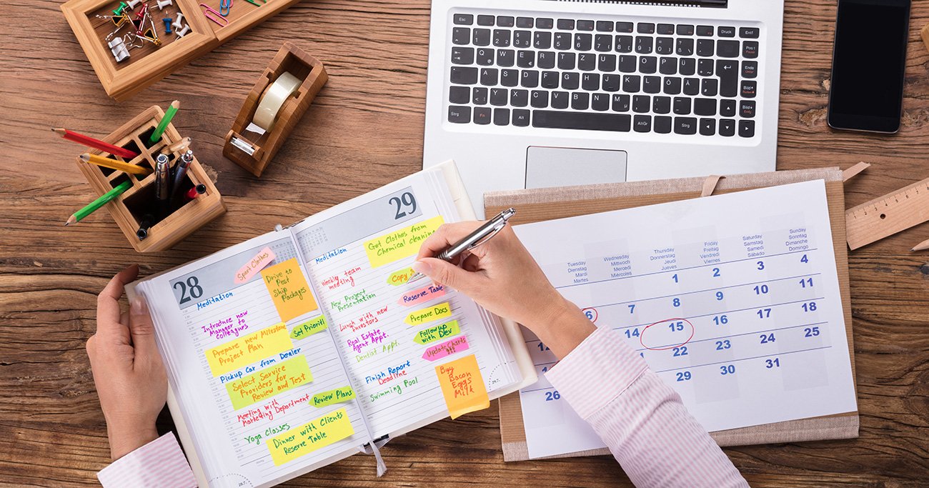  A person is seen using a laptop and a desk calendar to plan their schedule for the month.