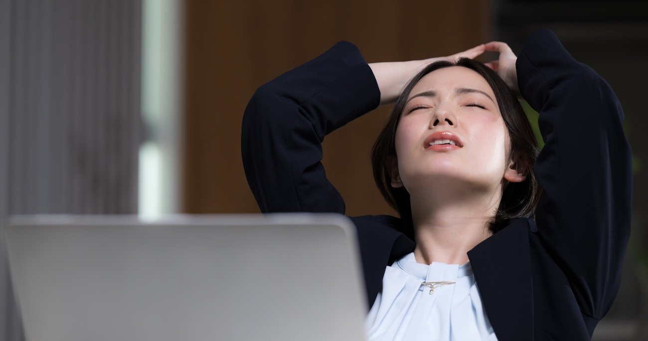 パソコンの前で天を仰いていでるスーツを着た女性