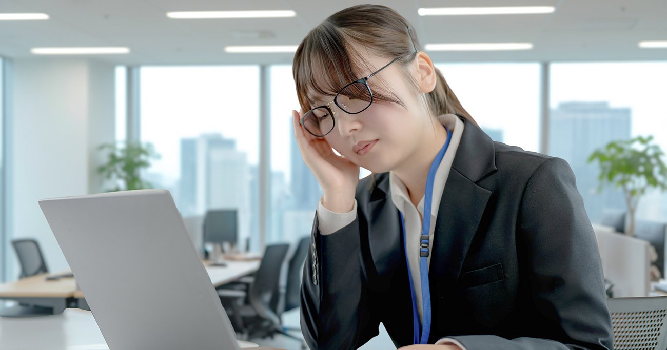 オフィスでパソコンを前にこめかみを押さえる女性