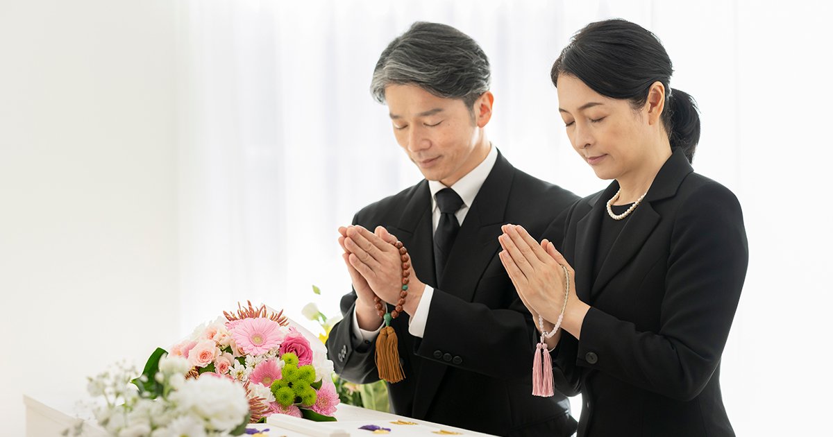 数珠を持って棺の前で手を合わせる喪服姿の男女