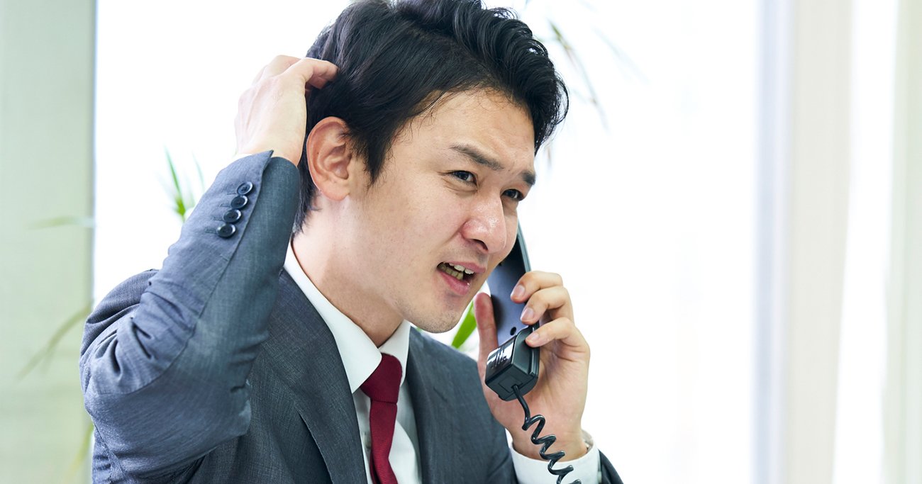 頭をかきながら電話をするビジネスパーソン