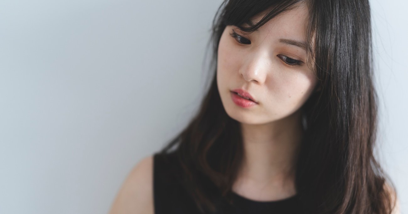 斜め下を物憂げに見る髪の長い女性。