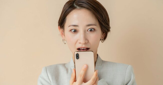 スマホ画面を見て驚く女性