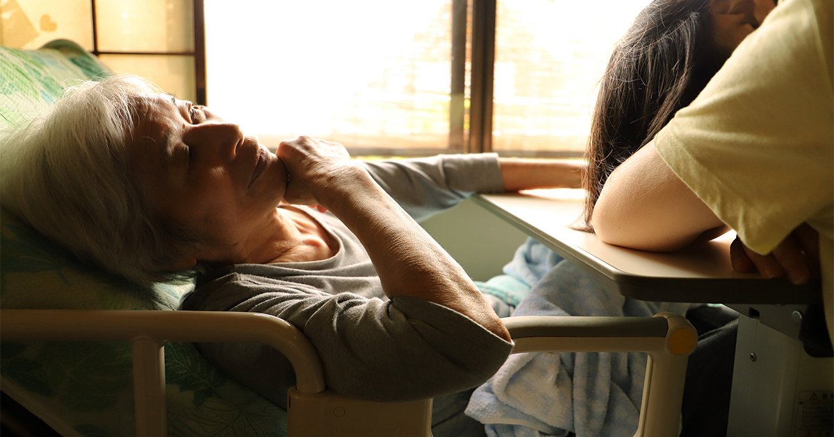 介護ベッドに横たわる年老いた母親と介護に疲れて眠り込む娘